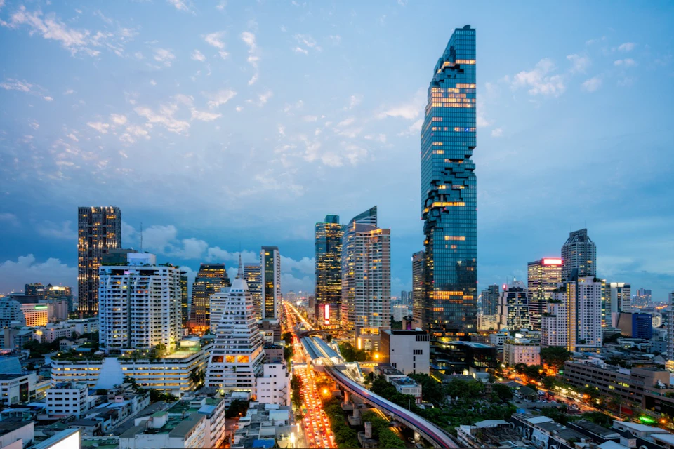 City skyline at dusk featuring a distinctive pixelated skyscraper and busy lit streets below.