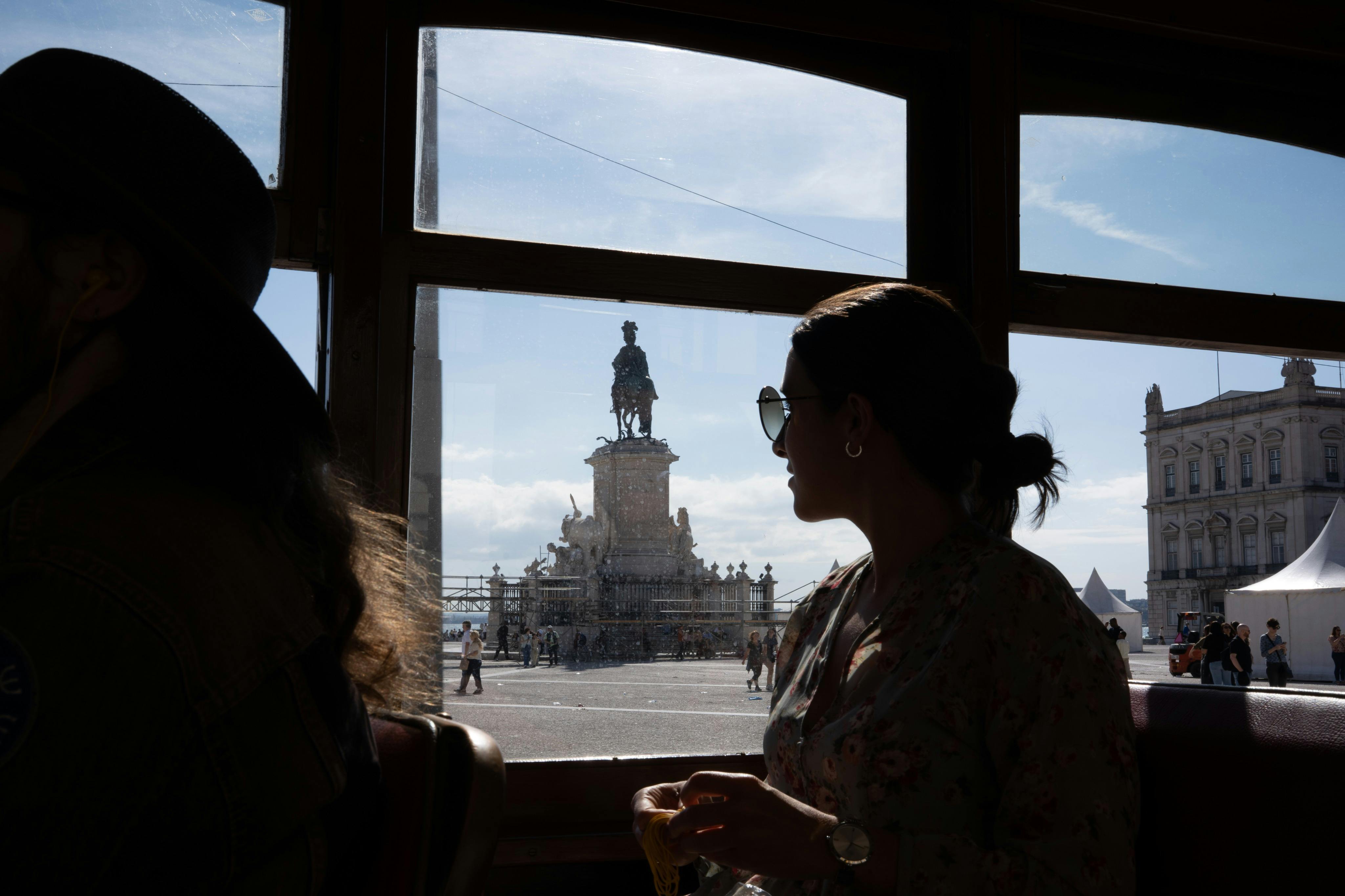 한 사람이 창문 근처 건물에 앉아 햇살이 내리쬐는 하늘 아래 공공 광장의 동상을 바라보고 있습니다.