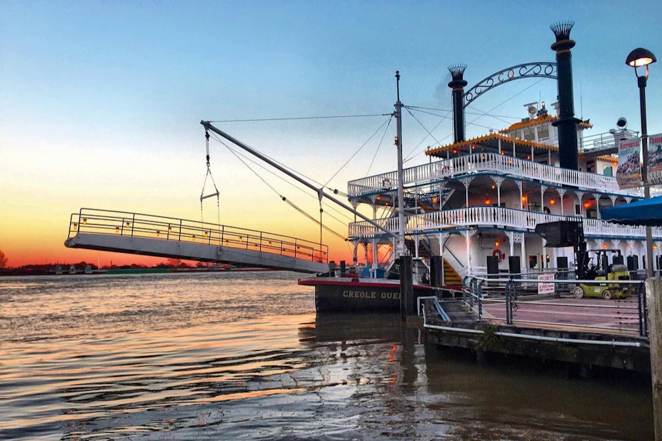 A docked paddlewheel steamboat named "Creole Queen" with sunset in the background and a raised boarding ramp on the left.