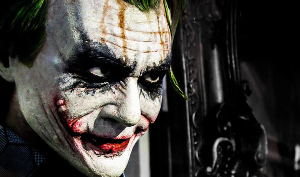 Close-up of a person in white face paint with smeared black eye makeup and red lips, resembling the Joker character.