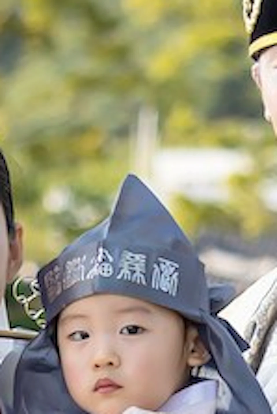 A family wearing traditional Korean Hanbok poses in front of a scenic background with traditional architecture and greenery.