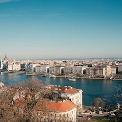 En stadsbild med en bred flod, historiska byggnader och en framträdande kupolformad struktur under en klarblå himmel.