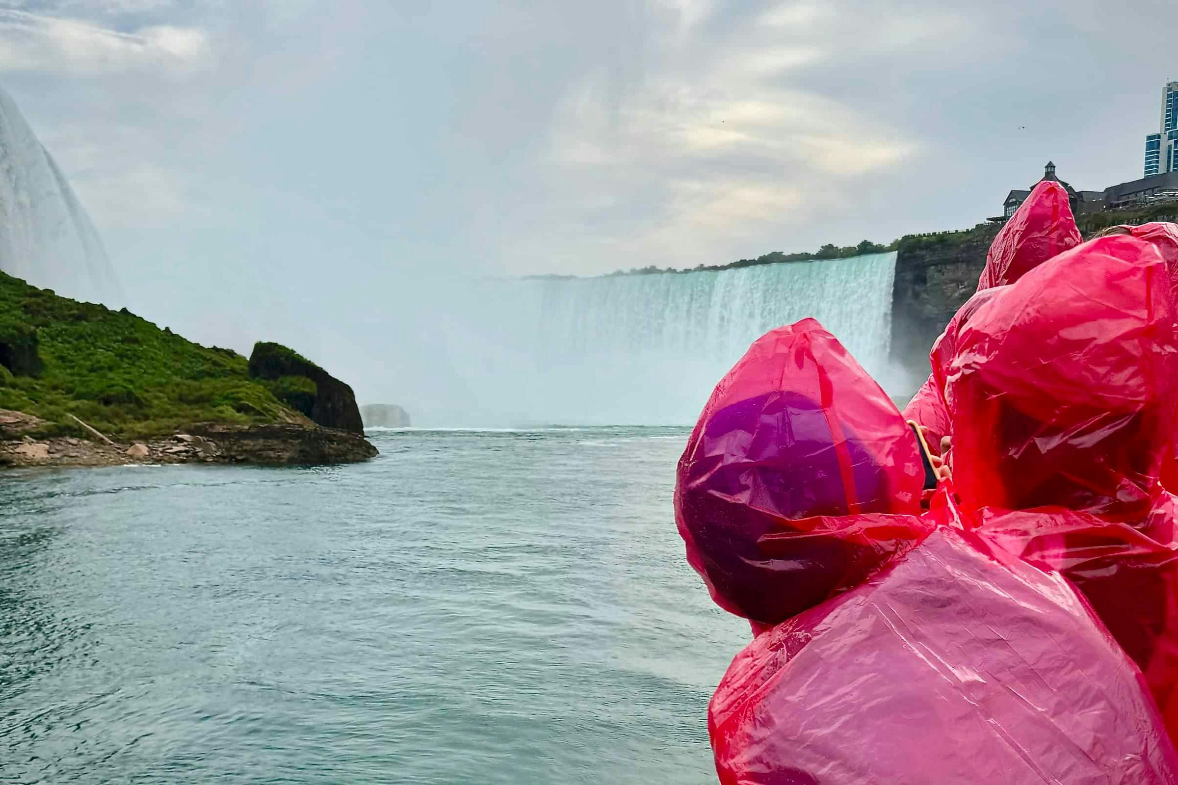 多人穿着红色雨衣站在船上欣赏壮观的尼亚加拉大瀑布。