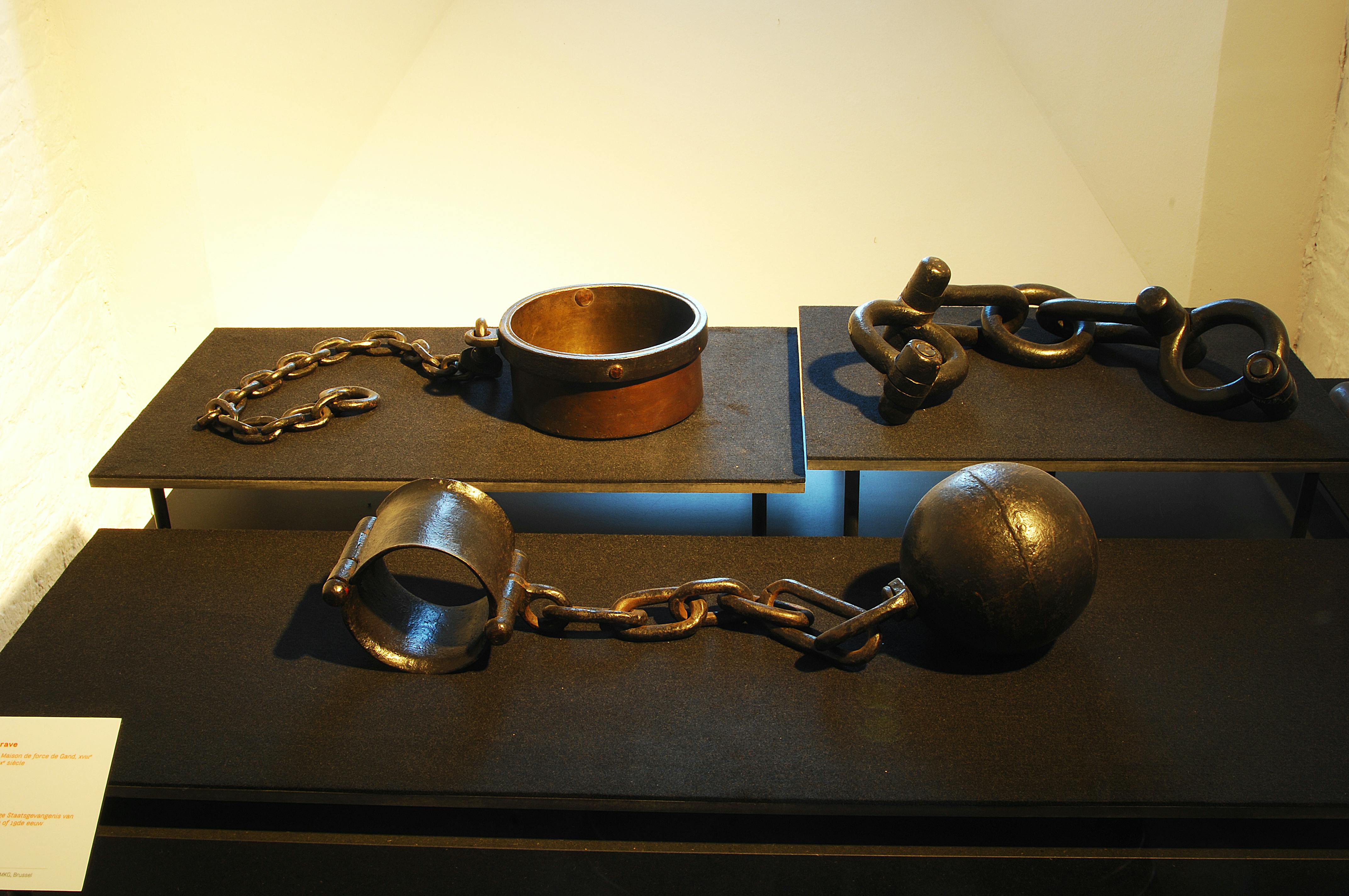 在昏暗的平台上展示历史悠久的镣铐和链条，背景昏暗。