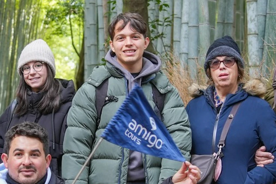 A group of people posing together in a bamboo forest pathway, some smiling and one holding a small flag.