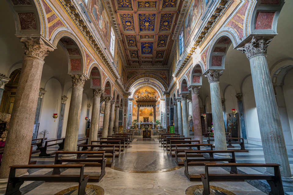 Interior of a richly decorated church with ornate columns, a vaulted ceiling, and rows of wooden pews leading to the altar.