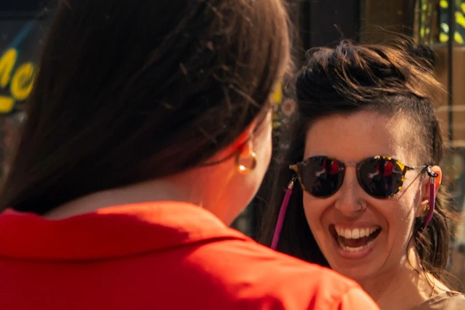 A guide in a red shirt interacts with smiling tourists in a lively urban area with flowers and pedestrians.