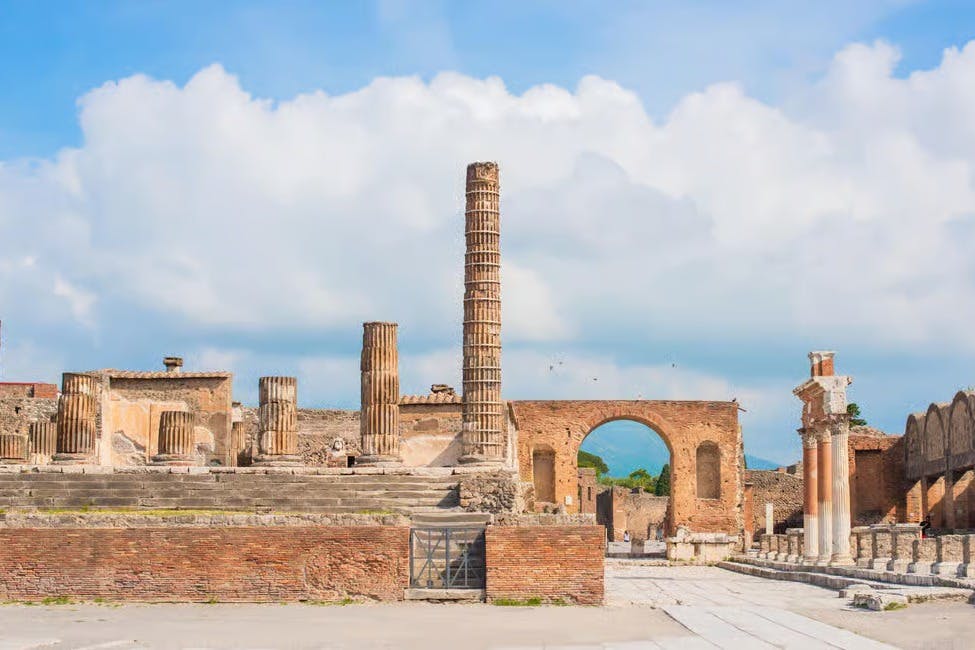 古代遗址，有几根柱子、石头结构和一个砖拱门，对着部分多云的天空。