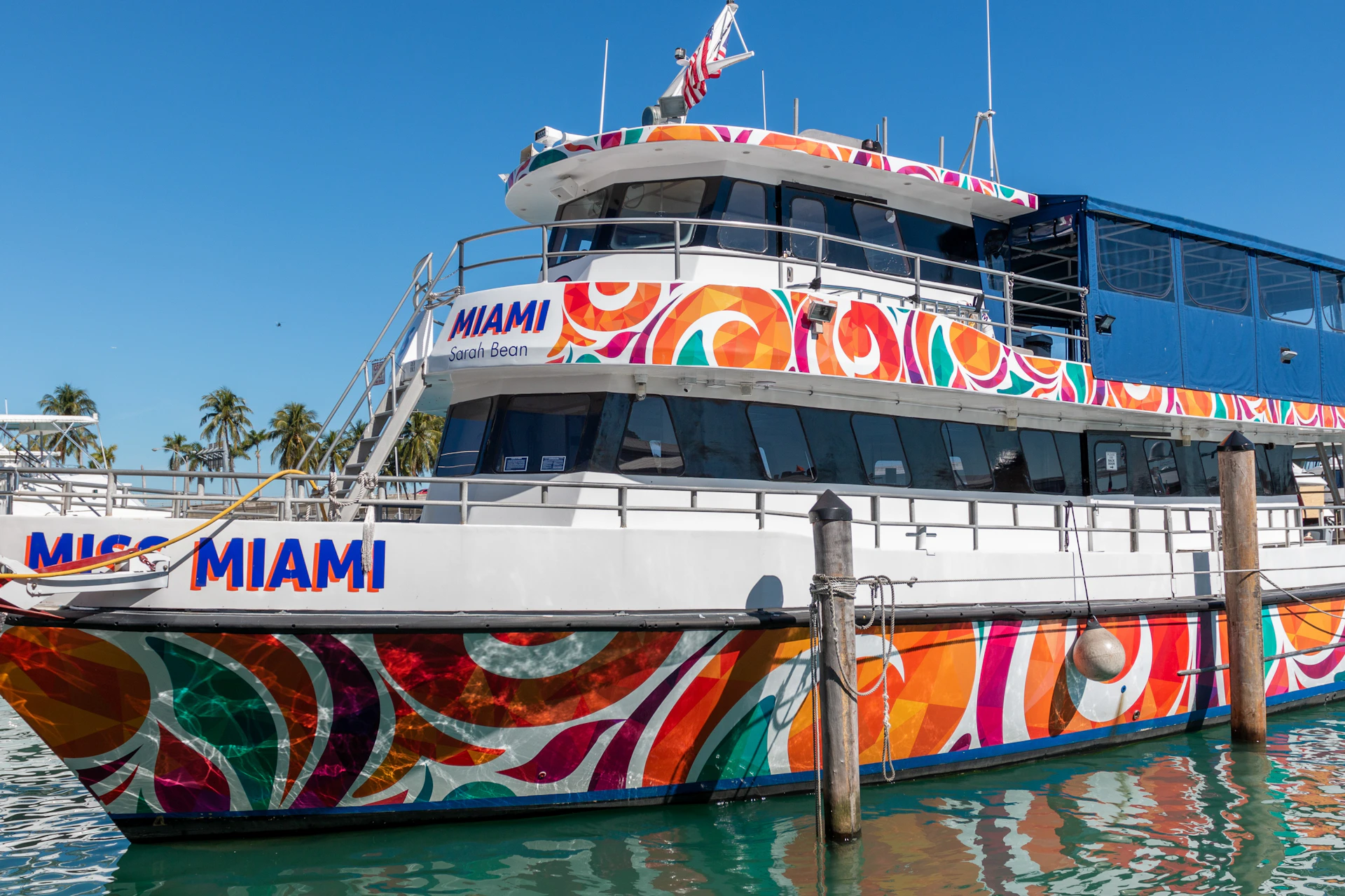 A colorful boat with vibrant patterns and the text "MIAMI" docked in a marina on a sunny day.