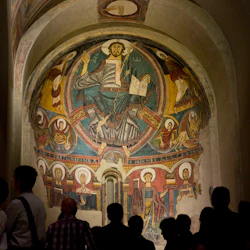 En grupp människor står framför en stor, invecklad religiös fresk inbäddad i en välvd vägg.