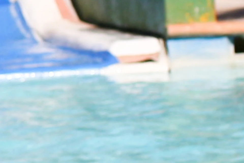 Three people in swimsuits enjoying a water park, standing in a pool at the bottom of colorful water slides, each with an inner tube.