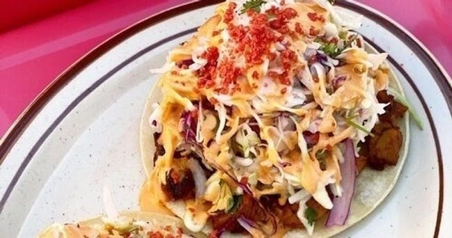 Gros plan d'un taco garni de légumes râpés, de sauce et de garniture émiettée sur une assiette.