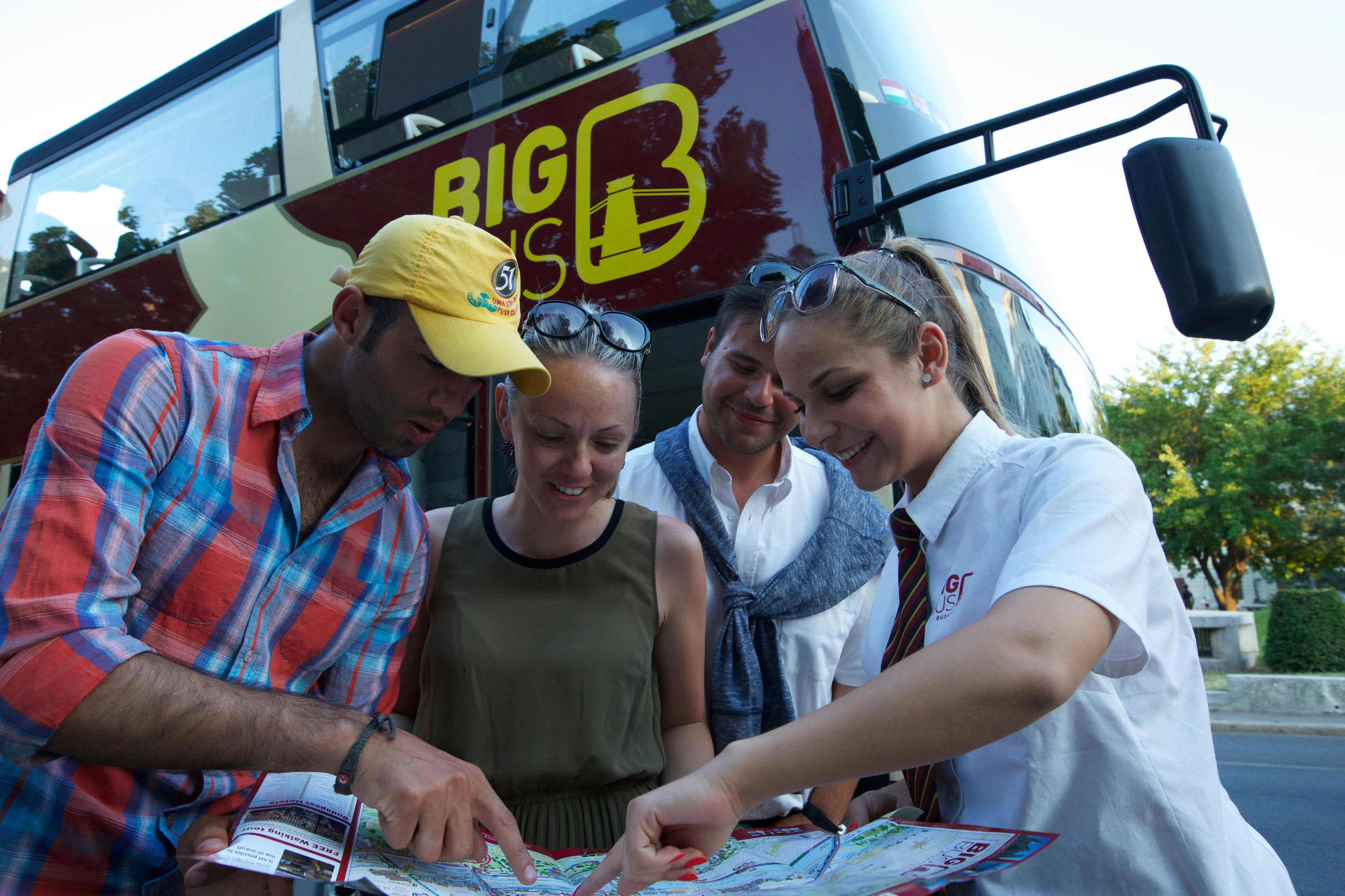 투어 가이드를 포함한 4명의 일행이 "빅 버스" 라고 표시된 관광 버스 근처의 지도를 보고 있습니다.