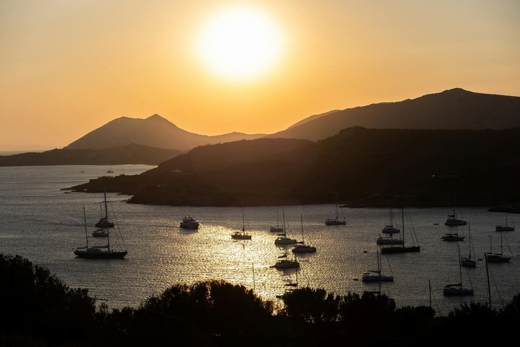 The Aegean Sea at sunset, with sailboats reflecting the golden glow near Cape Sounion.