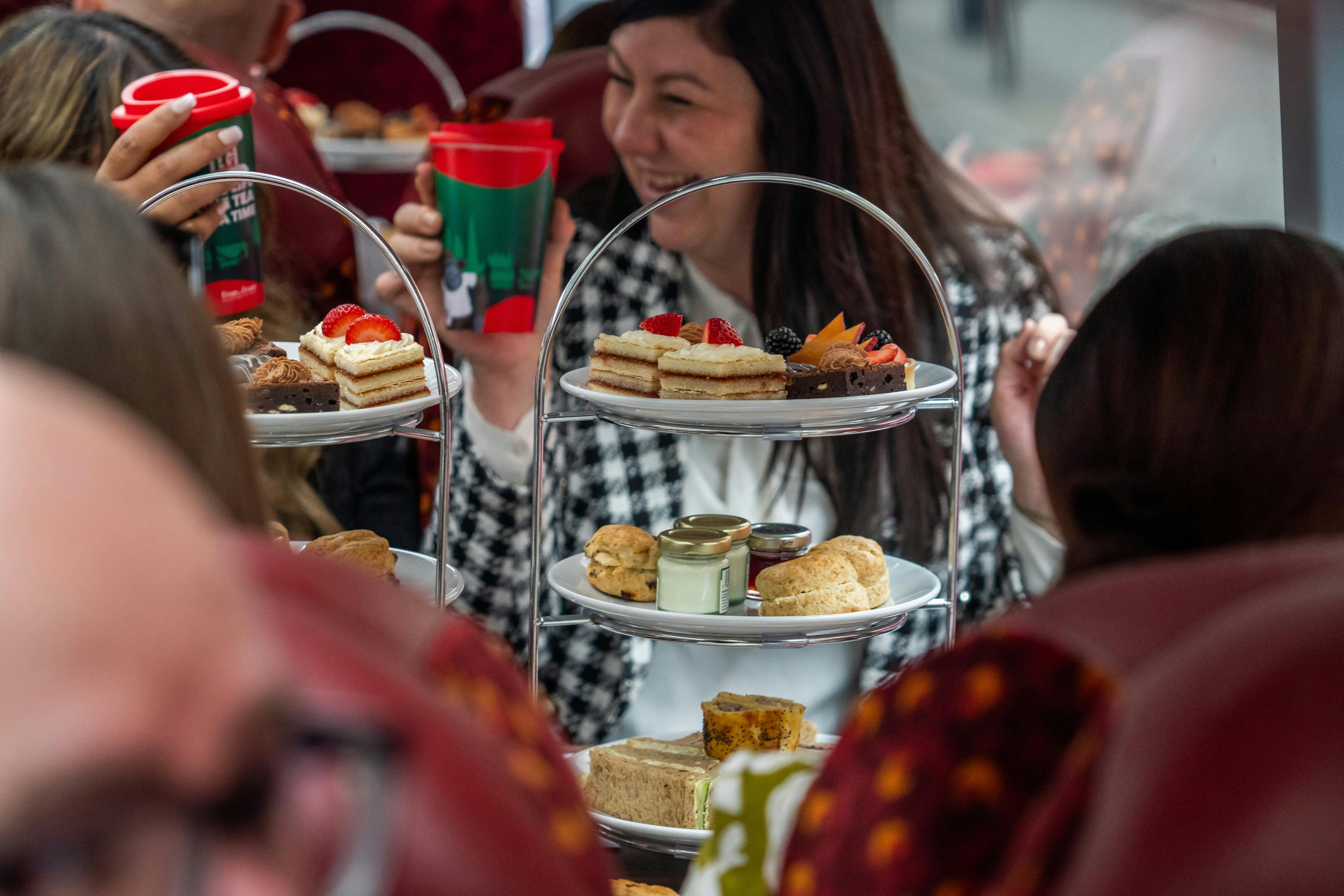 People enjoying an afternoon tea setup with tiered trays of snacks and festive red cups, in a social setting.