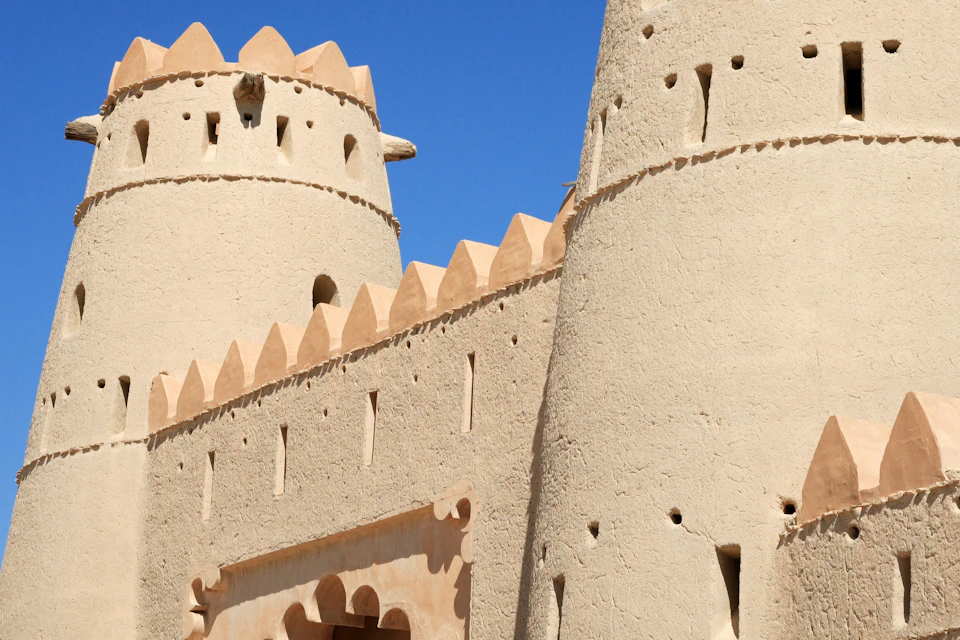 Close-up of an adobe fort with towers and decorative crenellations under a clear blue sky.