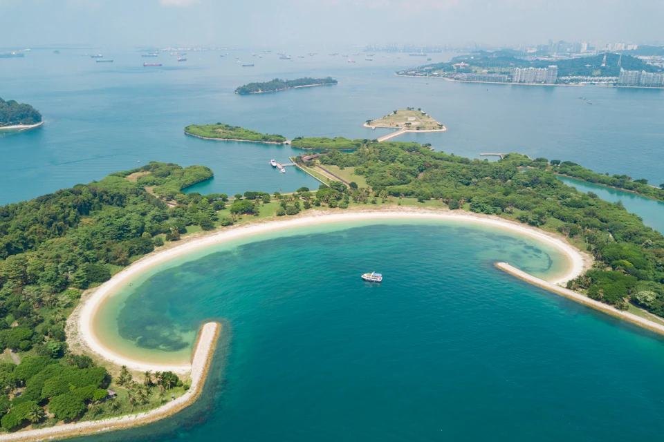 Aerial view of a tropical island with sandy beaches, lush greenery, and clear blue water, surrounded by smaller islands.