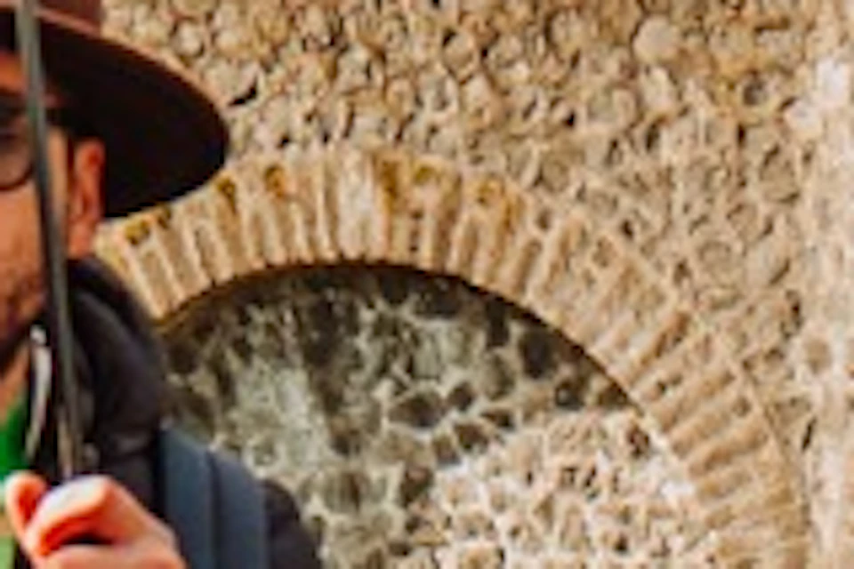 A tour guide holding an umbrella leads a group of tourists along a cobblestone pathway near ancient stone arches in sunlight.