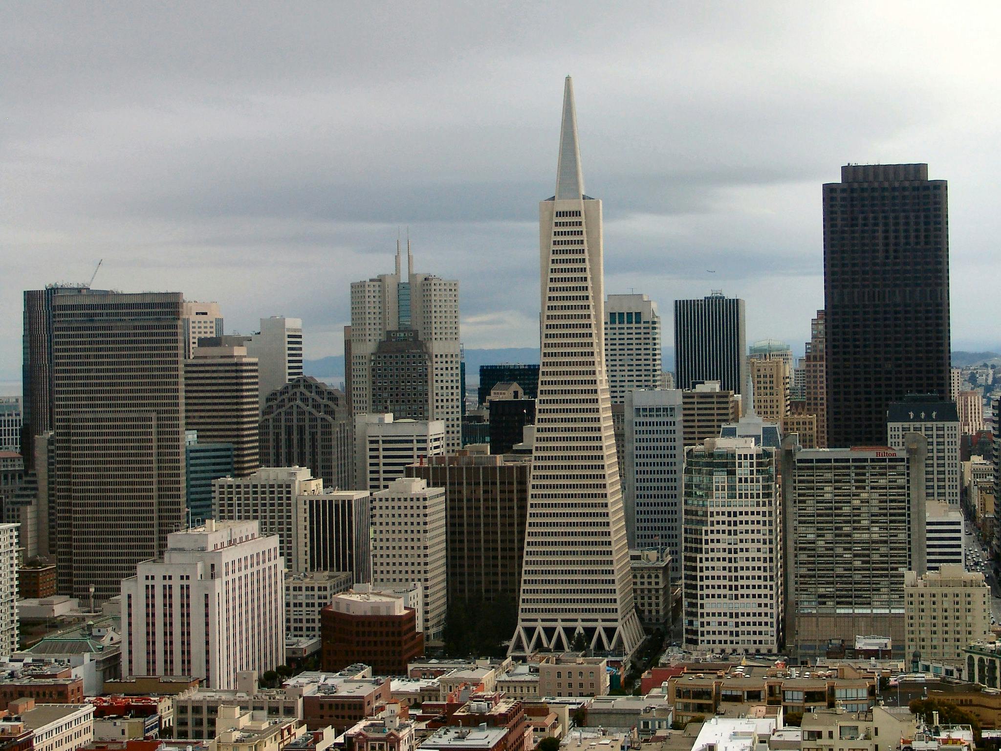 흐린 하늘 아래 중앙에 눈에 띄는 피라미드 모양의 마천루가 있는 수많은 높은 건물이 있는 도시 풍경입니다.