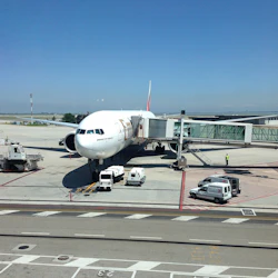 Ett stort plan anslutet till en jetbro vid en flygplatsgrind, med servicefordon och besättning på asfalten under en klar himmel.