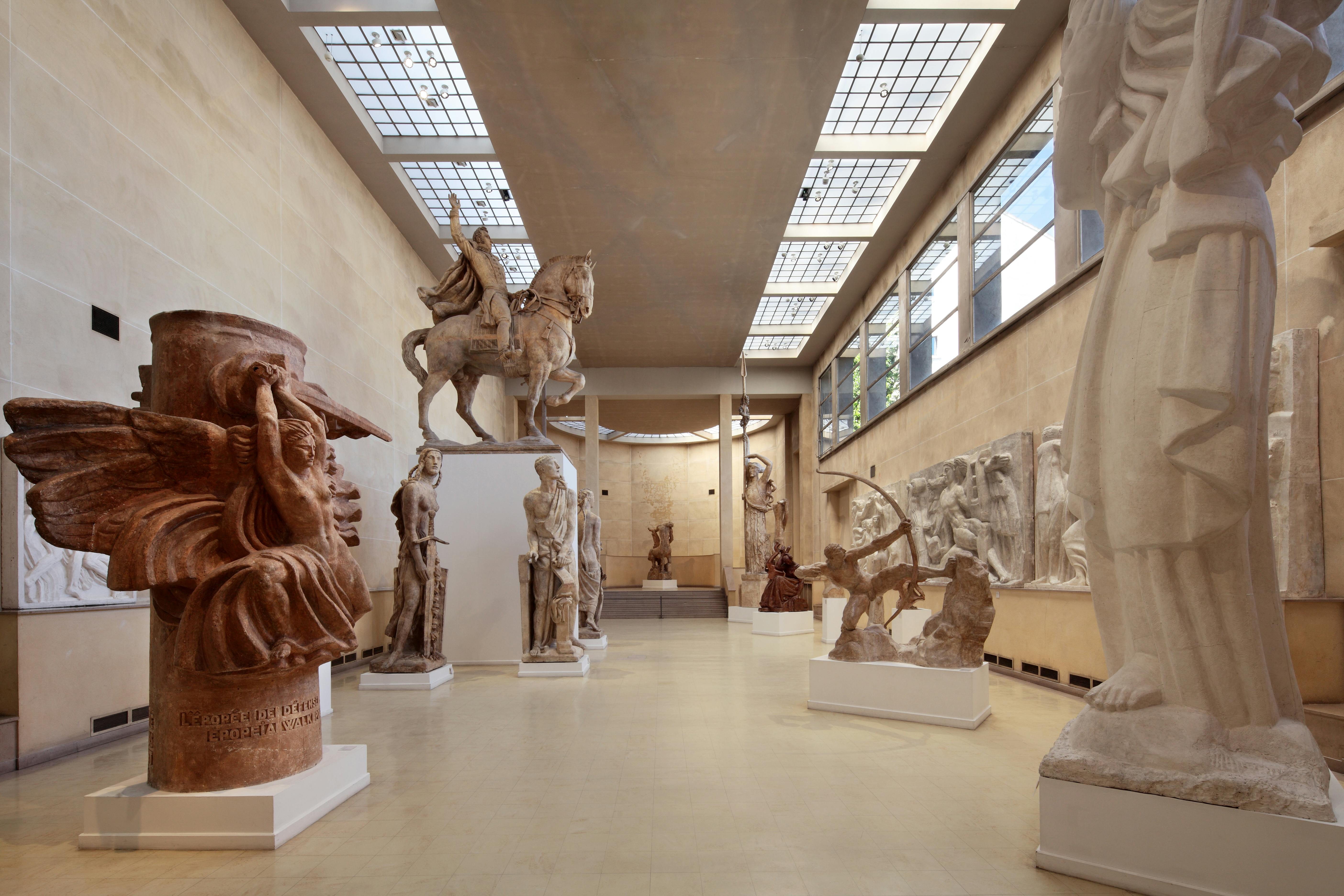 A museum hall displays various large classical sculptures, including statues of riders, warriors, and mythological figures.
