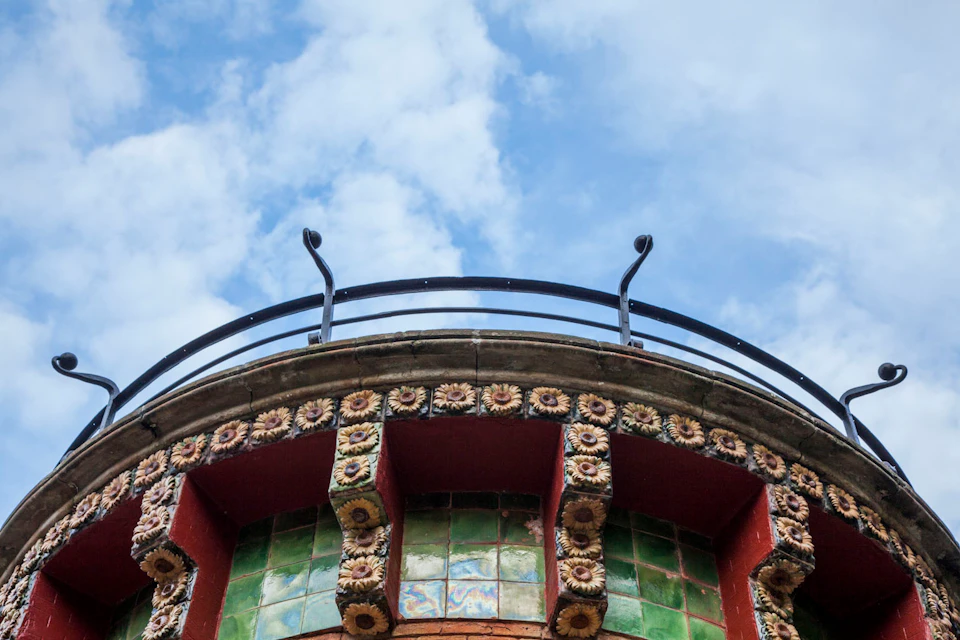 Decorative top of a building with intricate floral details and green tiles under a clear, partly cloudy sky.