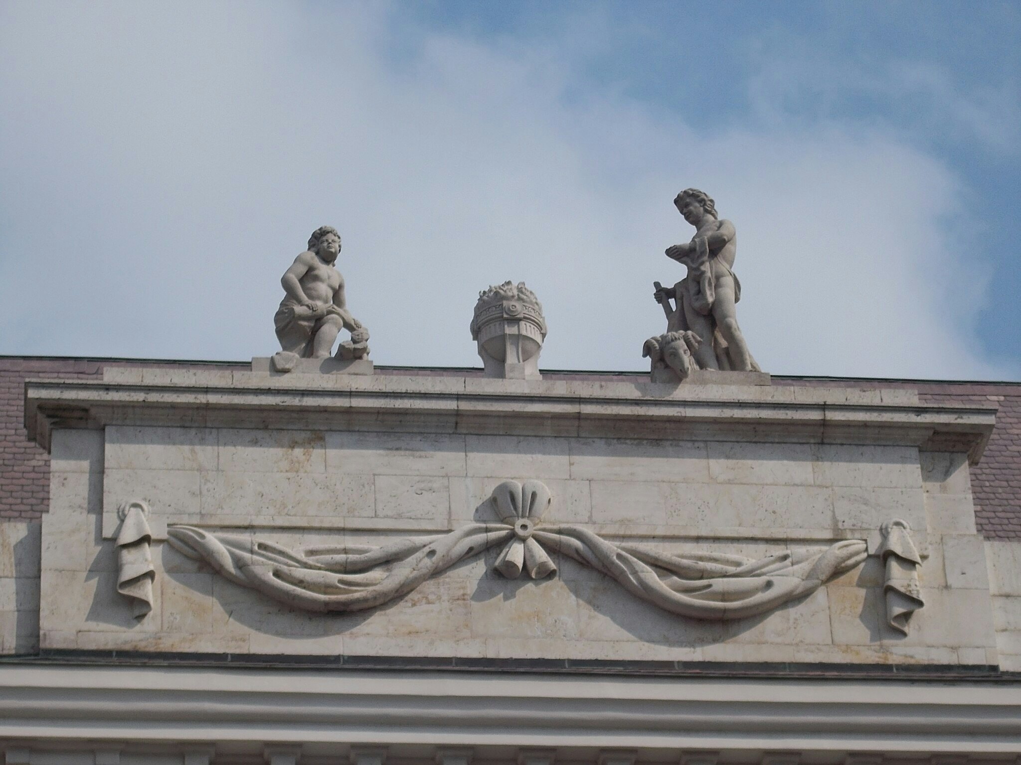 Stenstatuer af to figurer er placeret oven på en udsmykket bygningsfacade prydet med et draperet stofdesign.