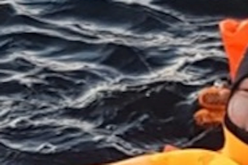 People wearing bright orange survival suits float on water, appearing relaxed and smiling.