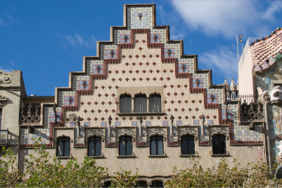 Ornate building facade with patterned tiles, arched windows, and a step-like roof design, set against a blue sky.