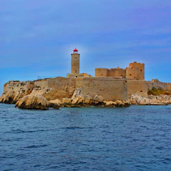 Stone fortress with a lighthouse on a rocky island, surrounded by blue ocean under a clear sky.