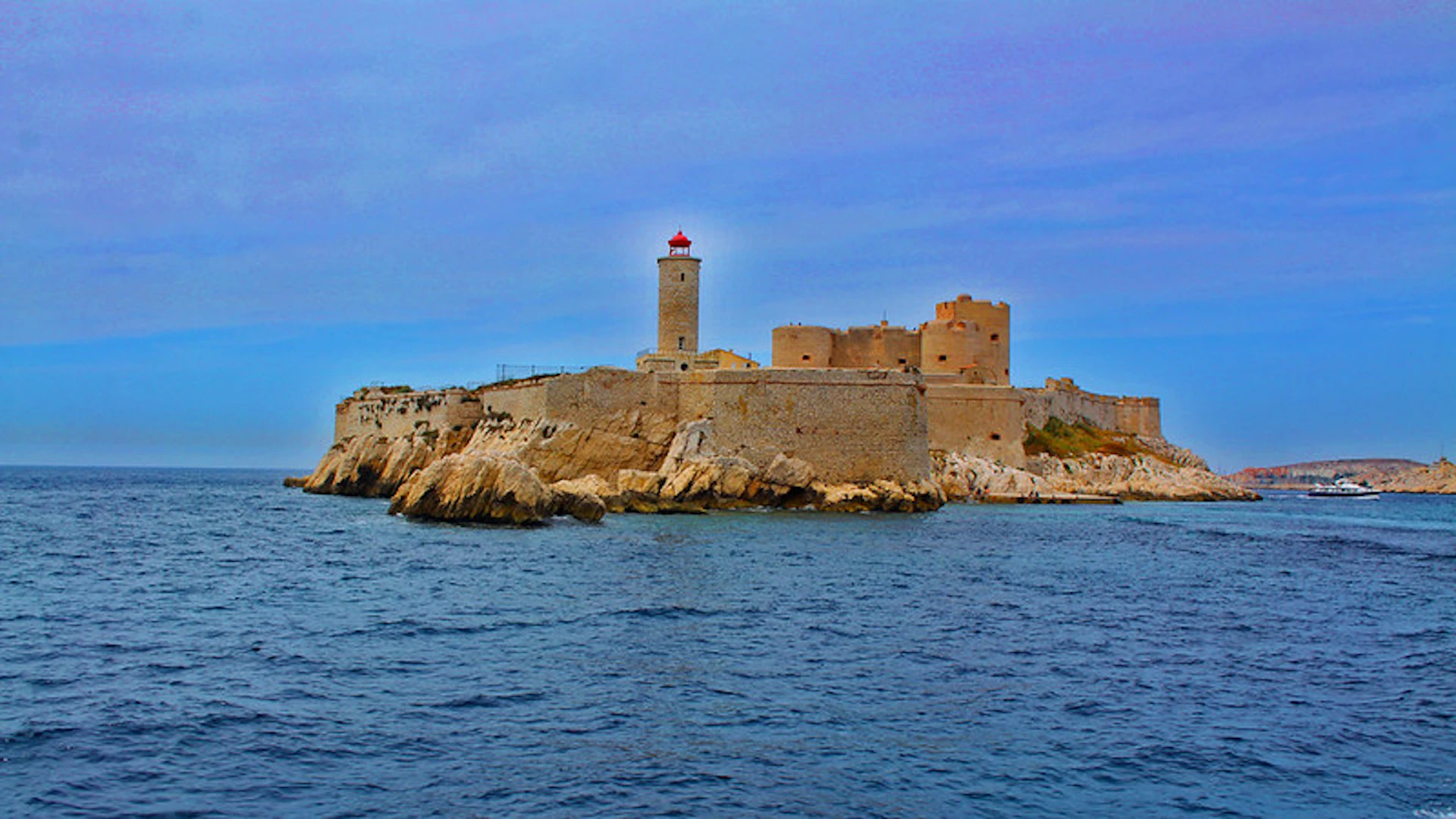 Stone fortress with a lighthouse on a rocky island, surrounded by blue ocean under a clear sky.