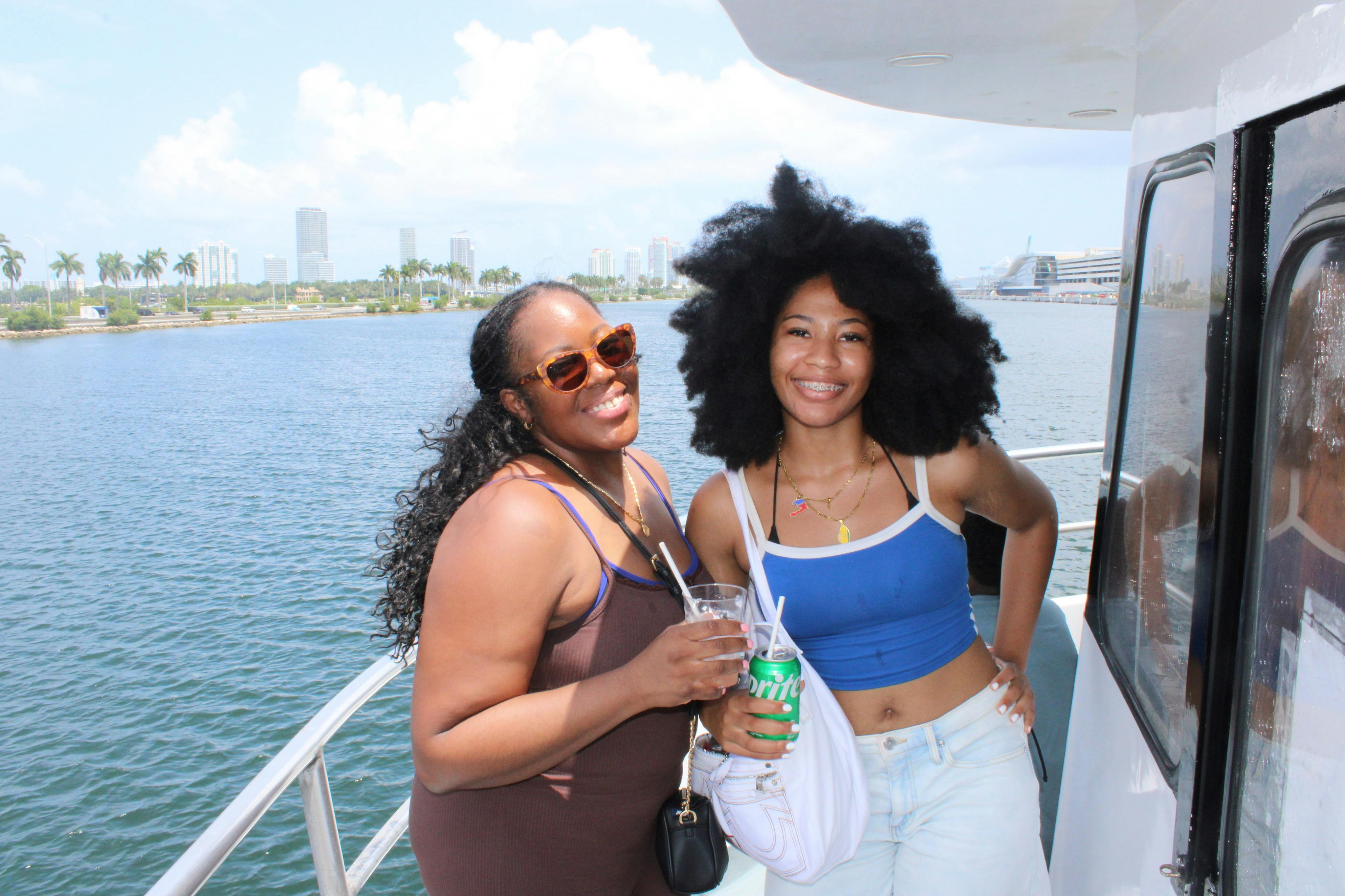Two women smiling on a boat with a city skyline and water in the background.
