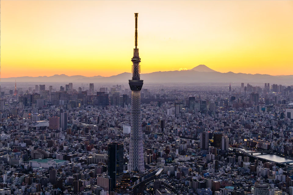 Tokyo skyline at dusk with the illuminated Tokyo Skytree in the foreground and Mount Fuji visible in the background.