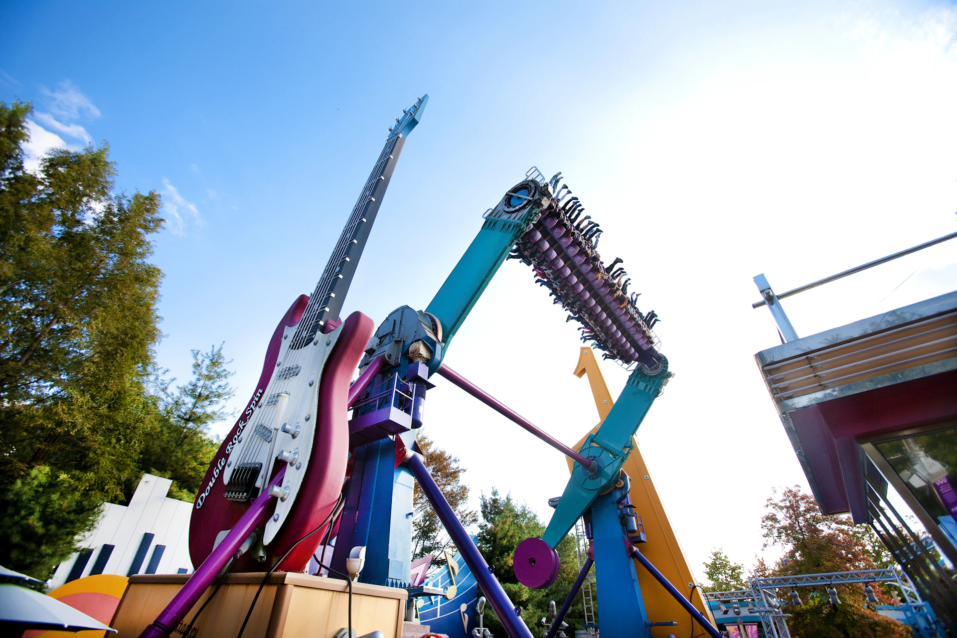 An amusement park ride shaped like a guitar with people riding on it, tilted at an angle against a clear sky.