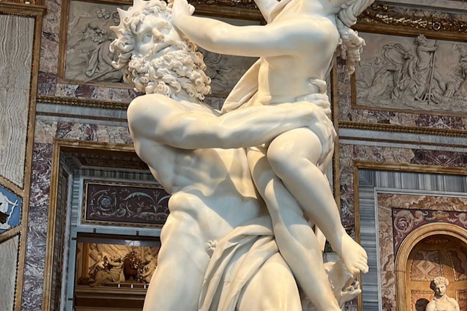A marble sculpture depicting a bearded man holding a smaller figure with intricate details, on display in a museum.