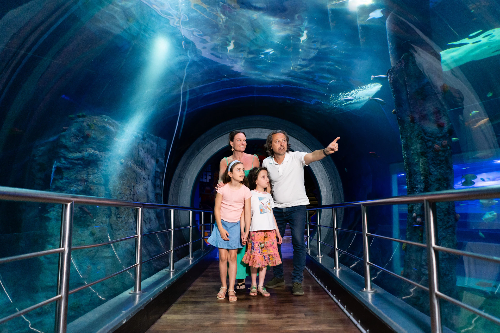 A family of four observing marine life in an underwater tunnel, with the father pointing at a fish.