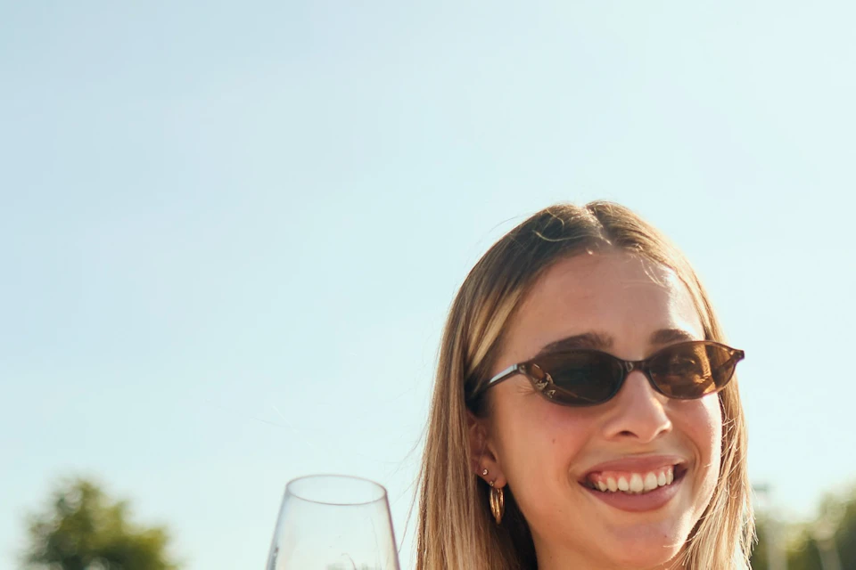 Three people enjoying drinks on a boat on a sunny day, with one person holding a wine glass and another holding a can.