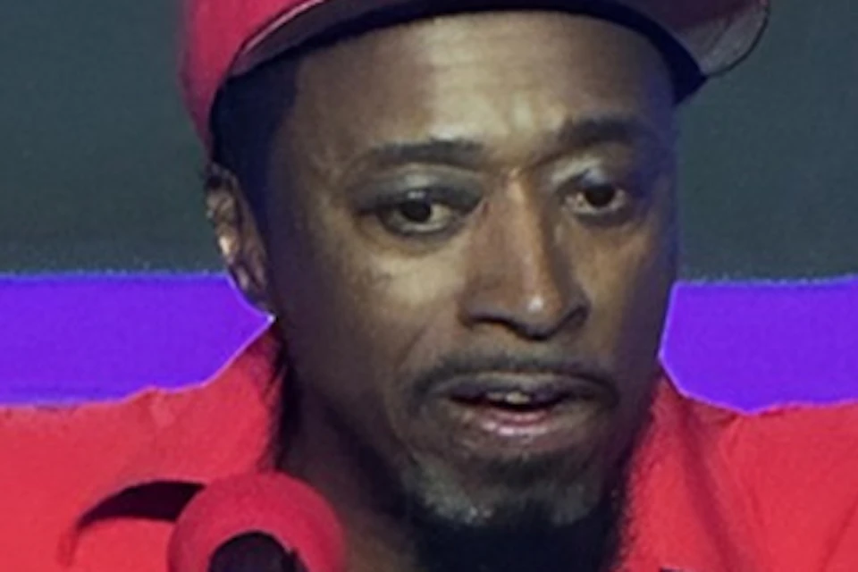 A person in a red outfit and cap performing on stage with a microphone stand in front of them.