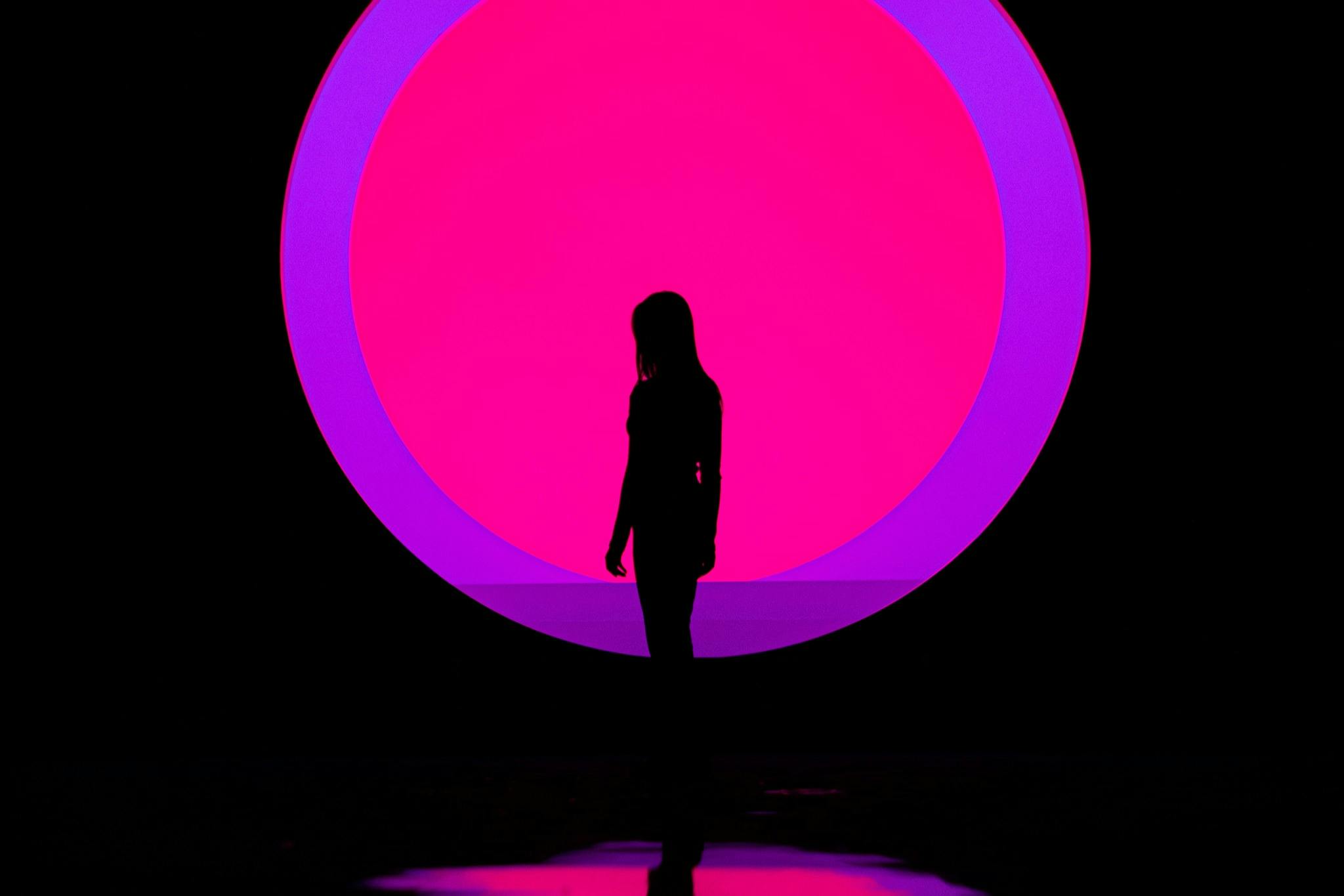 一个人站在明亮的粉红色和紫色圆形背景上的轮廓。