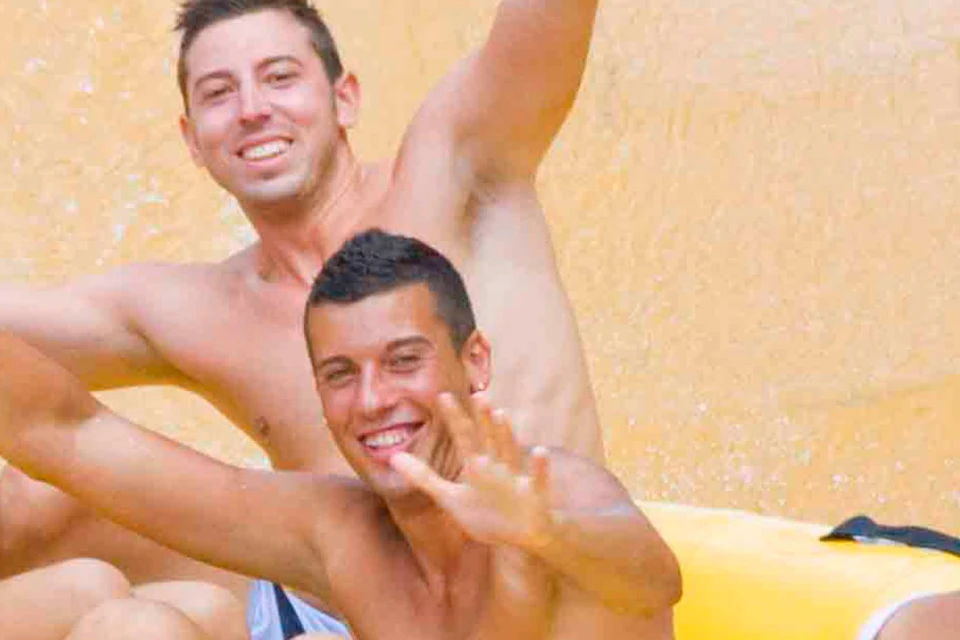 Four people are riding a yellow inflatable raft down a water slide, smiling and raising their arms in excitement.