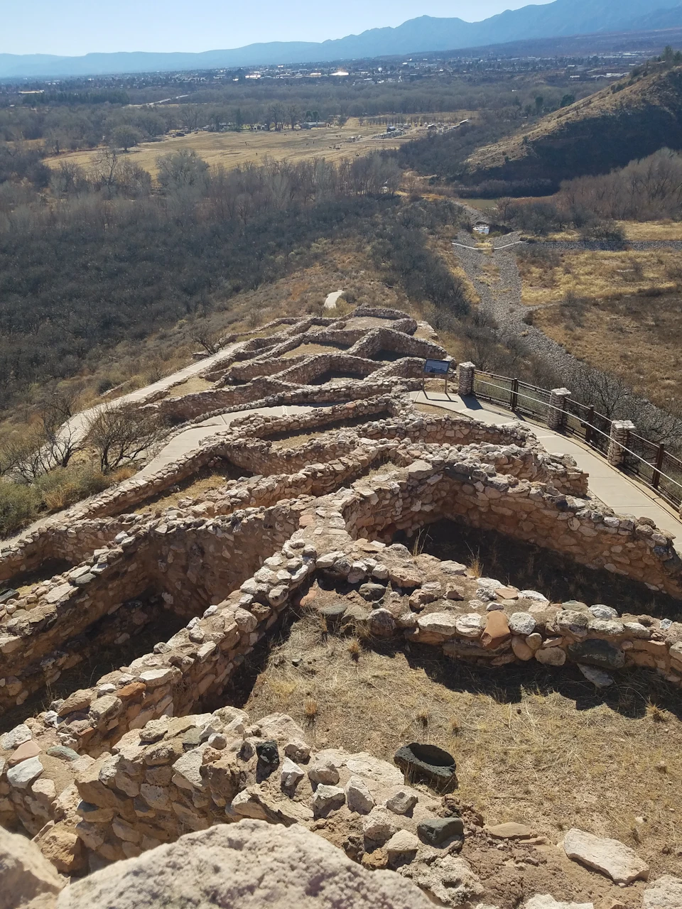Stone ruins of an ancient settlement on a hillside, with winding paths and dry vegetation surrounding the area.