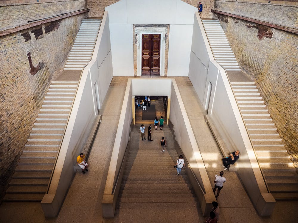 사람들이 오르내리는 커다란 내부 계단으로, 흰색 벽으로 둘러싸여 있으며 상단에 나무 문이 있습니다.