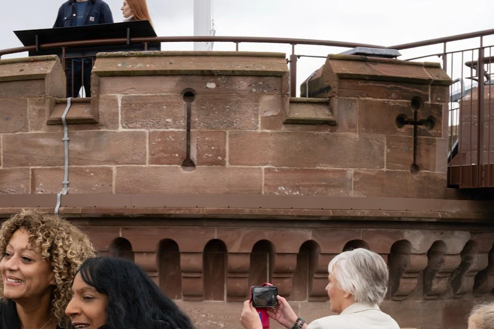 A group of people at a historical site with a stone turret and raised platform. Some are pointing, and one is taking photos.