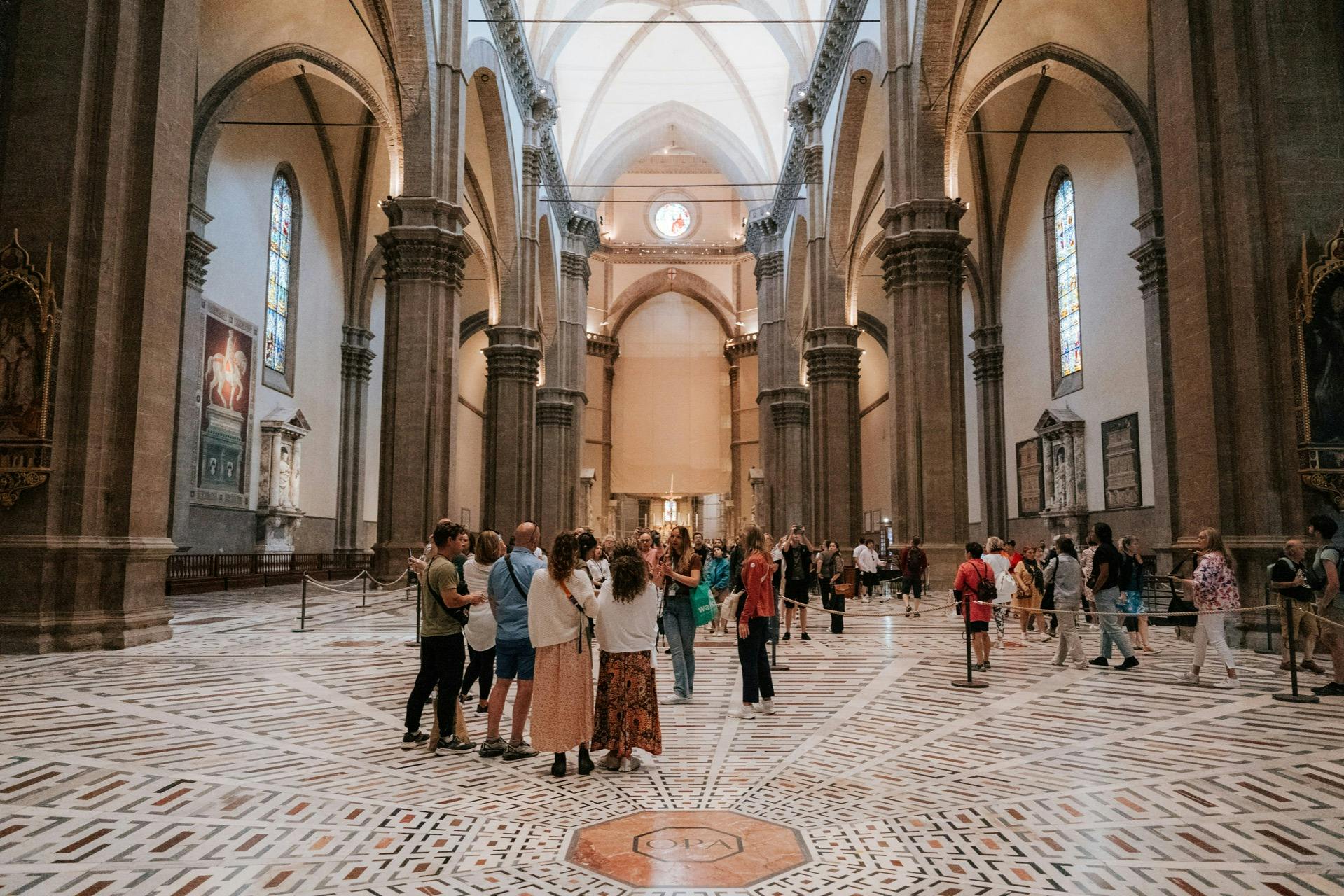 A group of people inside a grand cathedral with tall arches, intricate flooring, and stained glass windows.