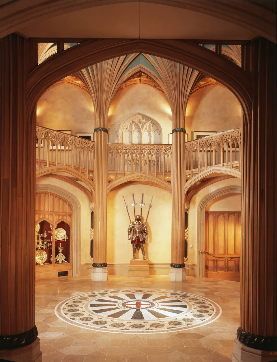 A grand hall with vaulted ceilings, ornate columns, a knight's armor display, and a circular tiled floor pattern.