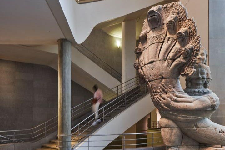 Velká kamenná plastika vícehlavého hada s lidskou postavou v muzejním prostředí se schodištěm v pozadí.