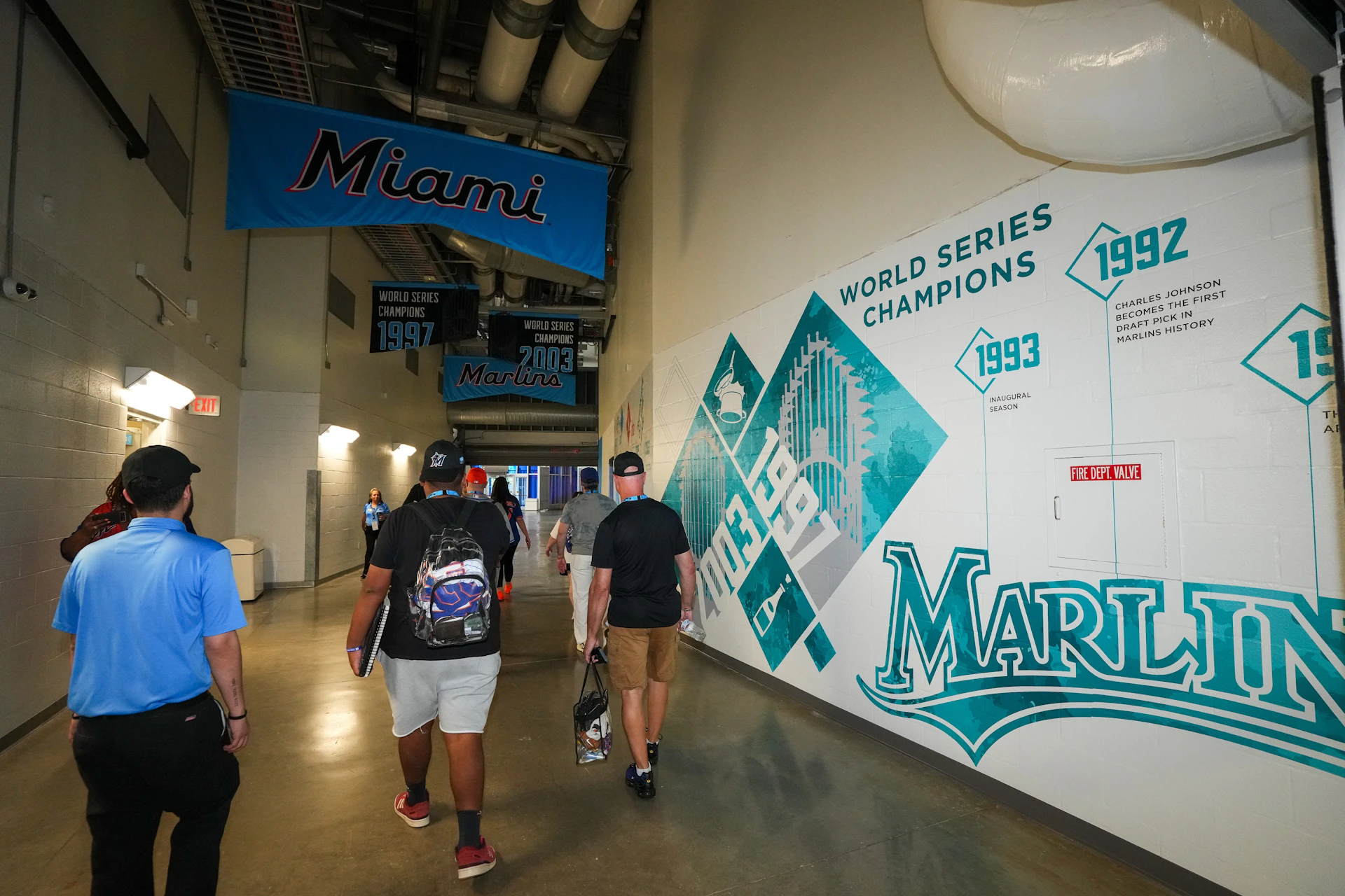 People walking through a hallway with Miami Marlins decorations, including banners and wall graphics about their championships.