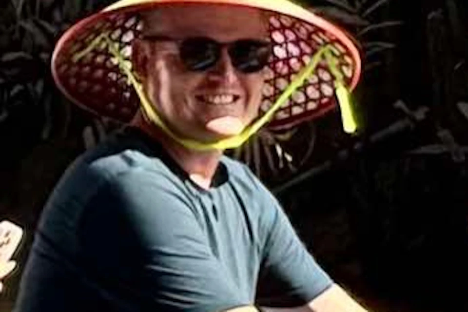 Three people wearing conical hats and sunglasses are seated in a blue and red boat, traveling through a tropical waterway.