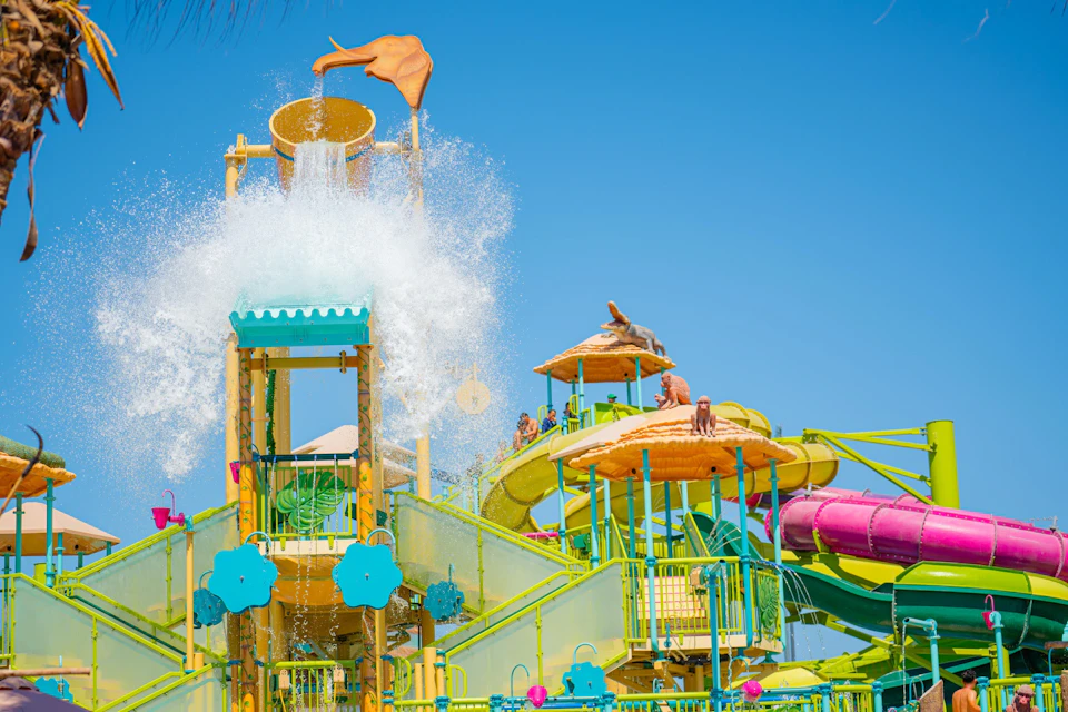 A colorful water park structure with slides and a large bucket spilling water under a clear blue sky.