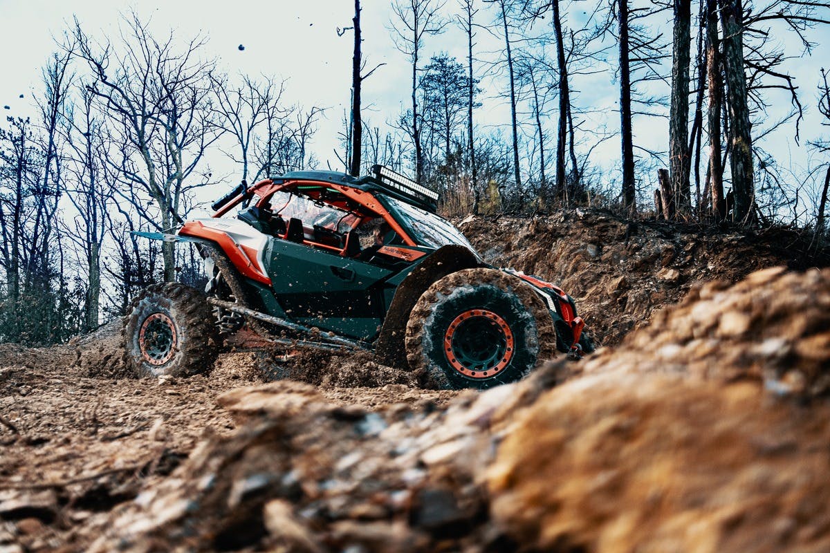 曇り空の下、裸の木々が生えた森の中、泥だらけの小道を走る頑丈なオフロード車。
